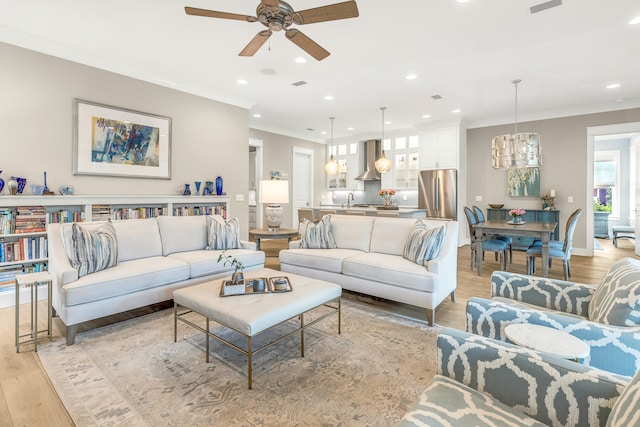 living room featuring ornamental molding, ceiling fan with notable chandelier, and light wood-type flooring