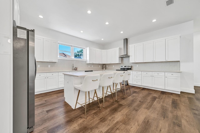 kitchen featuring backsplash, stainless steel appliances, dark hardwood / wood-style flooring, wall chimney exhaust hood, and a breakfast bar