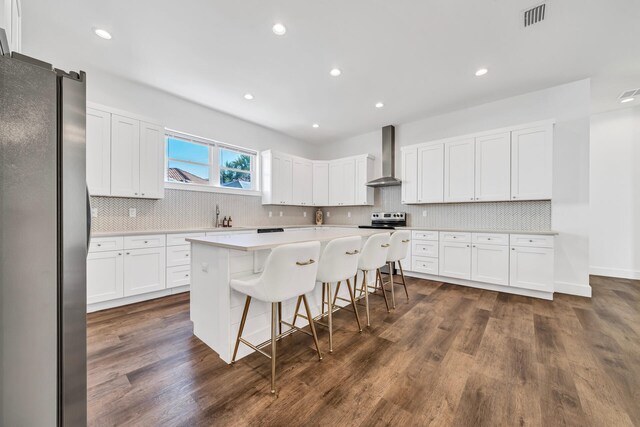 kitchen featuring stainless steel appliances, a kitchen breakfast bar, a kitchen island, dark hardwood / wood-style floors, and wall chimney exhaust hood