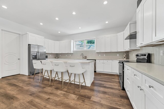 kitchen featuring range hood, a breakfast bar, dark hardwood / wood-style floors, appliances with stainless steel finishes, and white cabinets