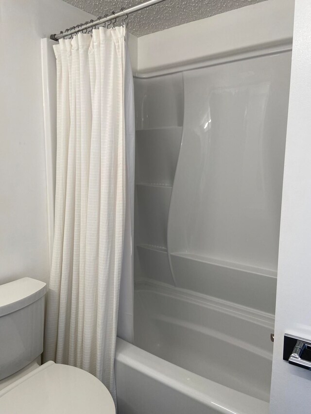 bathroom featuring shower / bath combination with curtain, toilet, and a textured ceiling