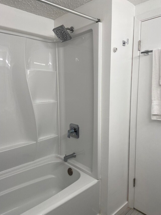 bathroom with washtub / shower combination and a textured ceiling