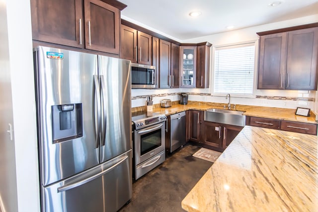 kitchen with appliances with stainless steel finishes, dark brown cabinets, sink, light stone counters, and tasteful backsplash