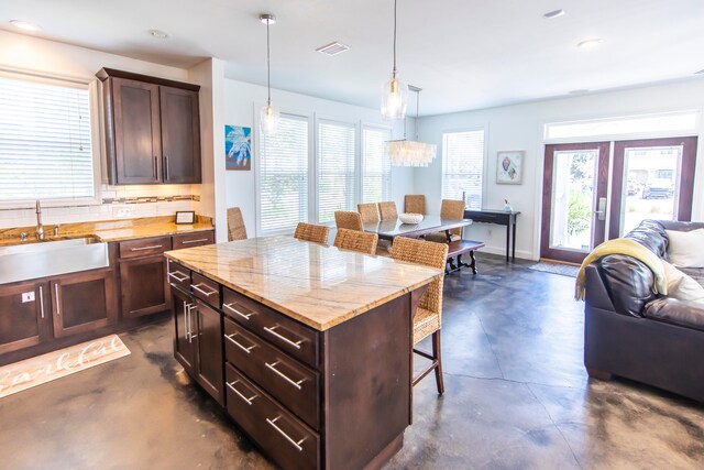 kitchen featuring hanging light fixtures, light stone countertops, sink, a breakfast bar area, and a kitchen island