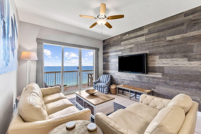 tiled living room featuring tile walls, wood walls, ceiling fan, and a water view