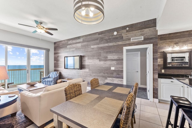 tiled dining area with tile walls, ceiling fan, and a water view