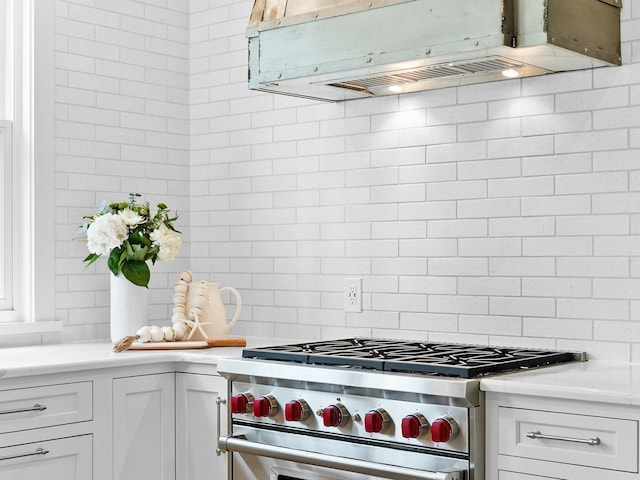 kitchen featuring light countertops, premium range hood, backsplash, white cabinets, and high end range