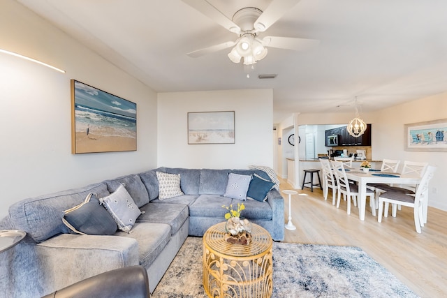 living room with ceiling fan with notable chandelier and light wood-type flooring