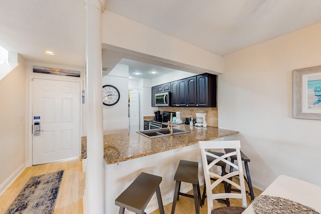 kitchen featuring a breakfast bar, light wood-type flooring, backsplash, stainless steel appliances, and light stone counters