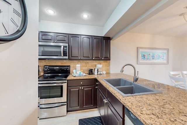 kitchen with light stone countertops, appliances with stainless steel finishes, sink, tasteful backsplash, and dark brown cabinetry