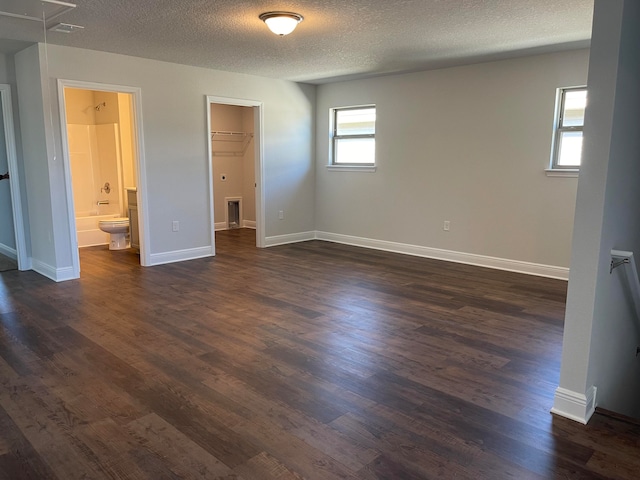 unfurnished bedroom featuring dark wood-type flooring, ensuite bathroom, a textured ceiling, and a walk in closet