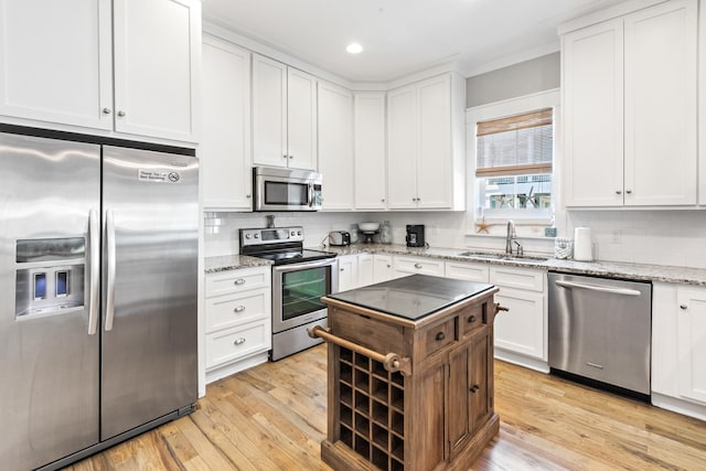 kitchen featuring appliances with stainless steel finishes, sink, light hardwood / wood-style floors, backsplash, and light stone countertops