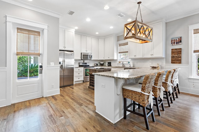 kitchen featuring light hardwood / wood-style floors, white cabinetry, hanging light fixtures, stainless steel appliances, and light stone countertops