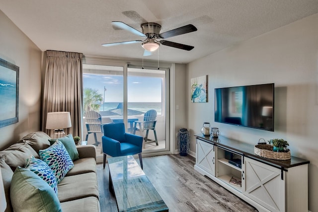 living room with ceiling fan, light hardwood / wood-style flooring, a textured ceiling, and a water view