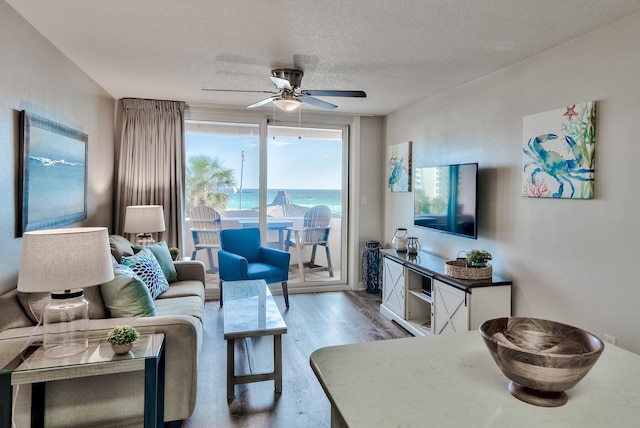 living room with a water view, a textured ceiling, ceiling fan, and light hardwood / wood-style floors