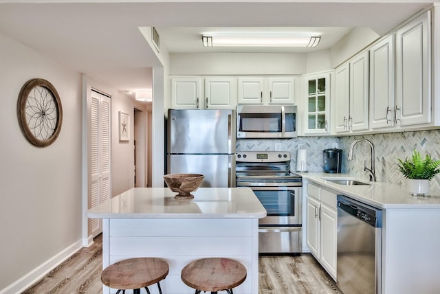 kitchen with light hardwood / wood-style flooring, backsplash, white cabinets, sink, and appliances with stainless steel finishes