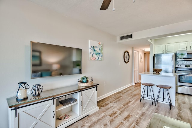 kitchen with light wood-type flooring, stainless steel appliances, a breakfast bar, tasteful backsplash, and ceiling fan