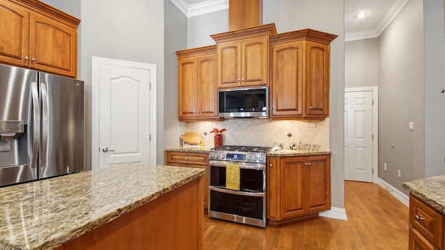 kitchen with backsplash, light hardwood / wood-style flooring, ornamental molding, light stone counters, and stainless steel appliances