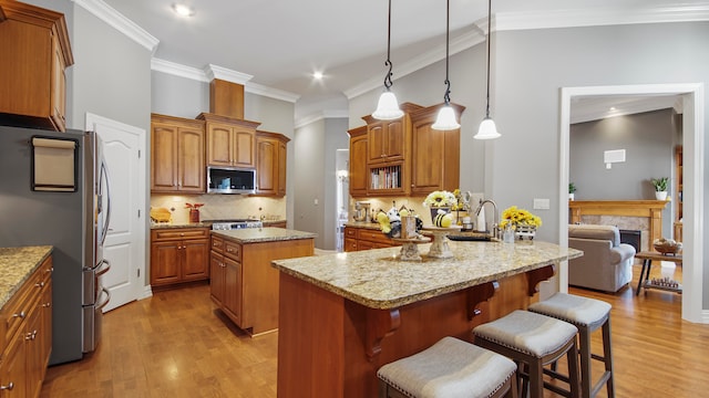 kitchen with appliances with stainless steel finishes, a kitchen island, ornamental molding, and light stone counters