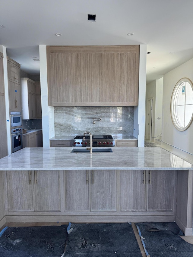 kitchen with light stone countertops, light brown cabinetry, a sink, and oven