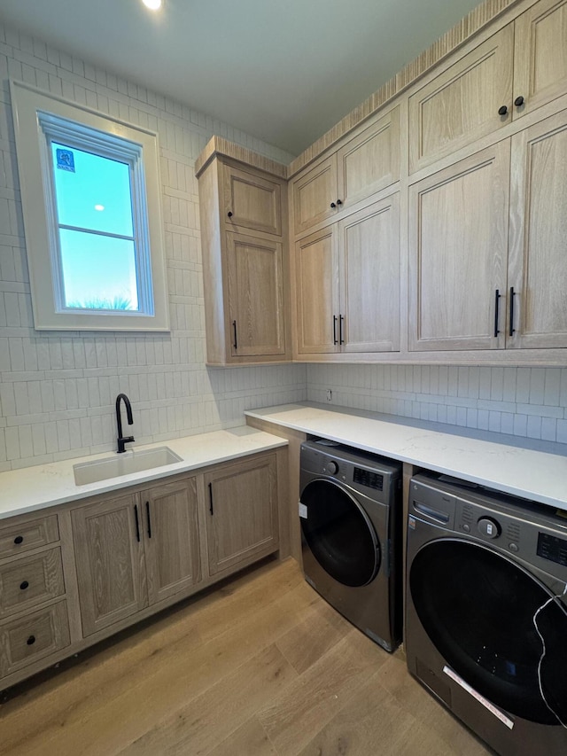 laundry area featuring cabinet space, light wood-style flooring, washer and clothes dryer, and a sink