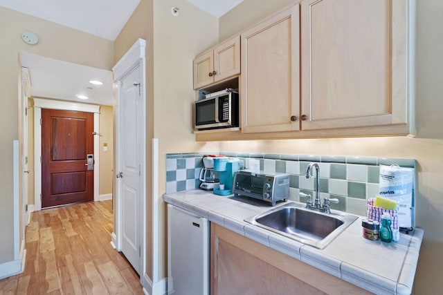 kitchen featuring light hardwood / wood-style floors, stainless steel microwave, tasteful backsplash, tile countertops, and sink