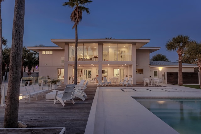 rear view of house featuring stucco siding, metal roof, fence, an outdoor pool, and a wooden deck