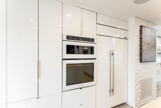 kitchen featuring paneled fridge, double oven, visible vents, white cabinets, and modern cabinets