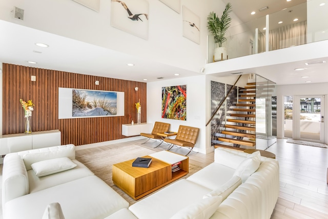 living room with a towering ceiling, an accent wall, stairs, wood walls, and recessed lighting