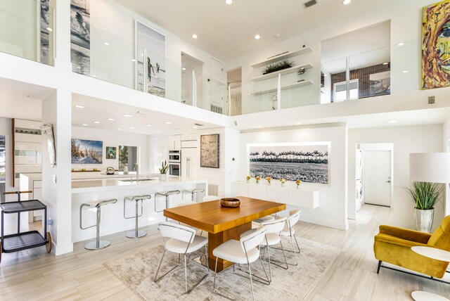 dining space featuring visible vents, light wood-style flooring, a towering ceiling, and recessed lighting