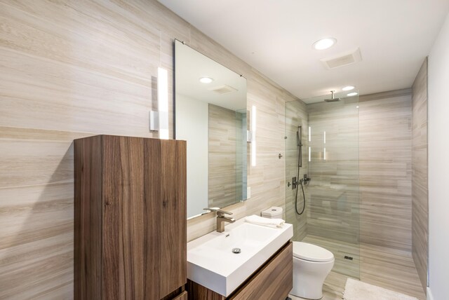 full bath with toilet, visible vents, vanity, tile walls, and a tile shower