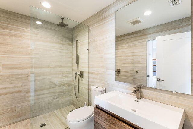 full bathroom featuring tile walls, visible vents, toilet, vanity, and a walk in shower