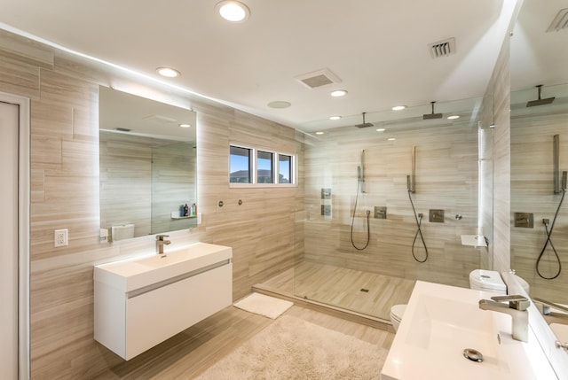 full bath with tile walls, visible vents, toilet, a tile shower, and vanity