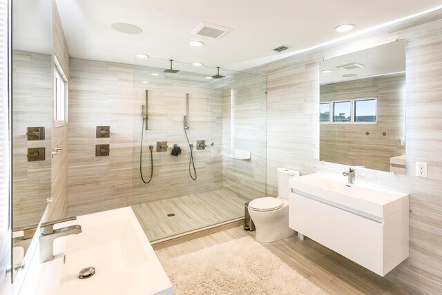 full bath with visible vents, toilet, a tile shower, vanity, and tile walls