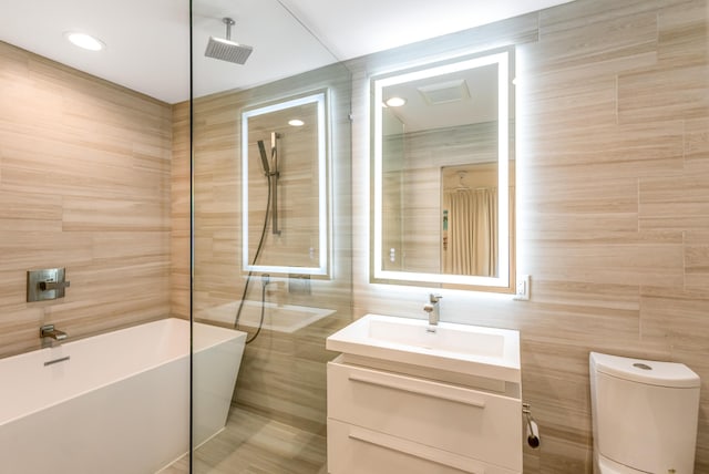 full bath featuring a freestanding bath, toilet, vanity, and tile walls