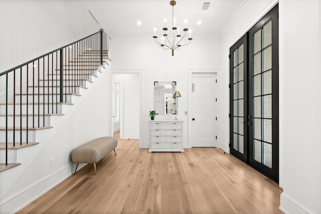 foyer featuring french doors, crown molding, light wood-type flooring, and a chandelier