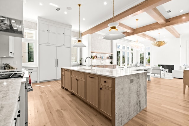 kitchen featuring sink, light wood-type flooring, decorative light fixtures, high end stainless steel range, and a large island