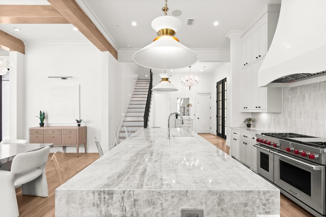 kitchen featuring range with two ovens, premium range hood, a kitchen island with sink, and sink