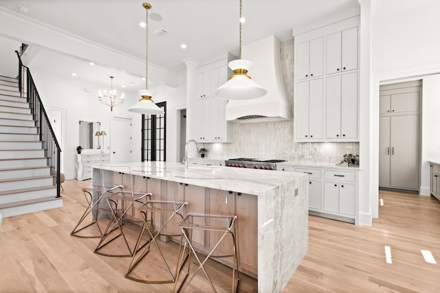 kitchen with light stone counters, custom exhaust hood, a spacious island, and light wood-type flooring