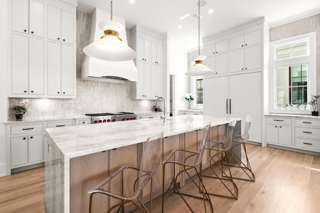 kitchen featuring hanging light fixtures, a center island with sink, light wood-type flooring, and white cabinetry