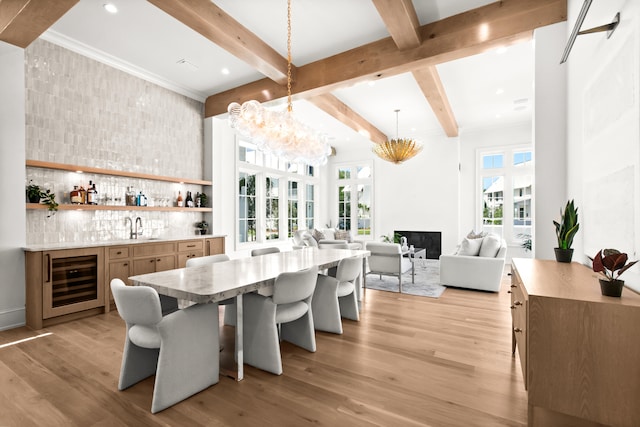 dining room featuring wine cooler, a large fireplace, an inviting chandelier, sink, and light hardwood / wood-style floors