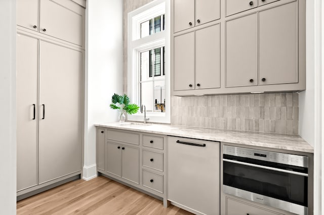 kitchen with oven, sink, tasteful backsplash, light wood-type flooring, and white dishwasher