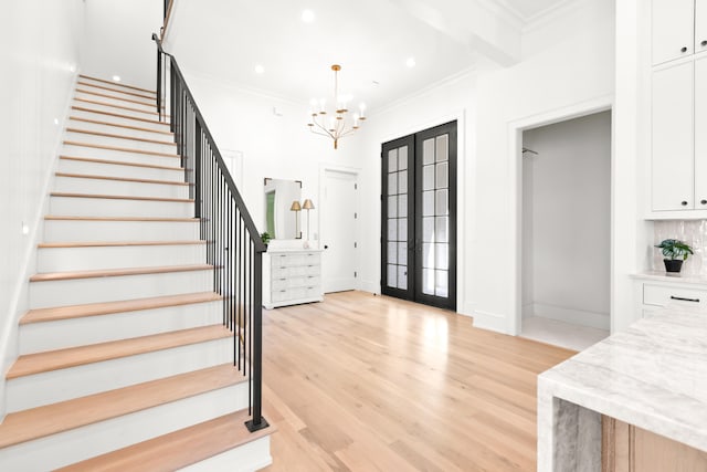 foyer entrance featuring french doors, an inviting chandelier, ornamental molding, and light wood-type flooring