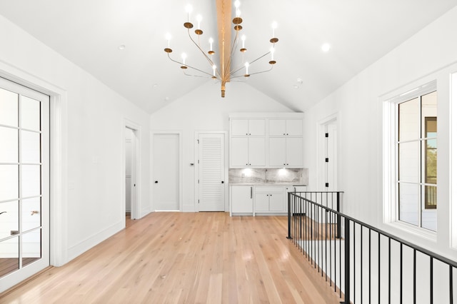 interior space with a healthy amount of sunlight, light hardwood / wood-style flooring, high vaulted ceiling, and a notable chandelier