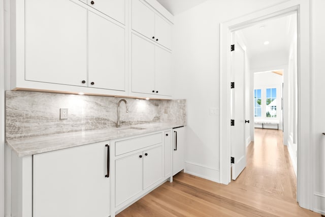 kitchen featuring white cabinetry, backsplash, light hardwood / wood-style floors, light stone counters, and sink