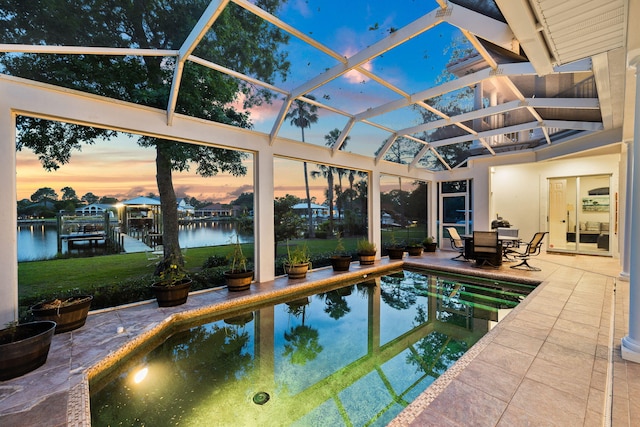 pool at dusk featuring a patio, glass enclosure, and a water view