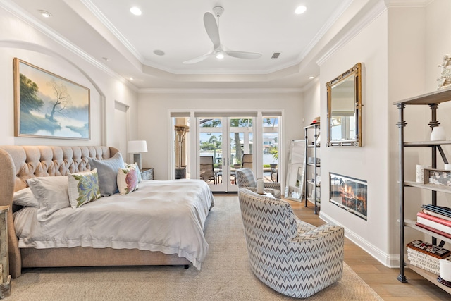 bedroom with ceiling fan, crown molding, access to exterior, a tray ceiling, and hardwood / wood-style flooring