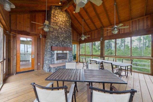 sunroom / solarium featuring vaulted ceiling with beams, ceiling fan, a stone fireplace, and wood ceiling