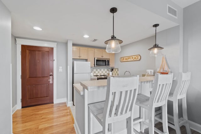 kitchen featuring white fridge, light hardwood / wood-style floors, tasteful backsplash, pendant lighting, and a breakfast bar