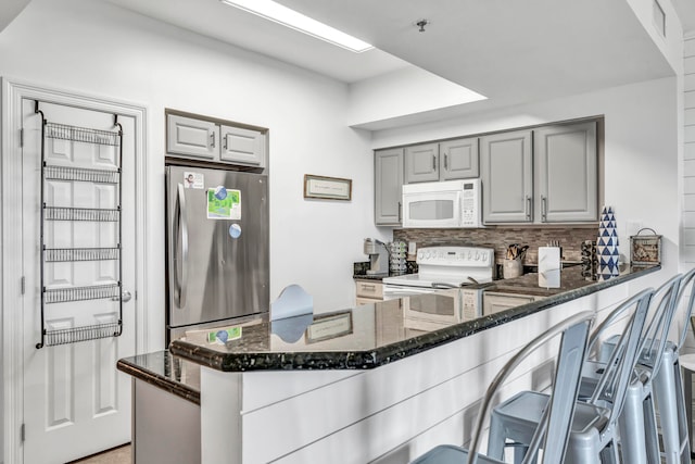 kitchen with kitchen peninsula, a kitchen breakfast bar, dark stone counters, gray cabinetry, and white appliances